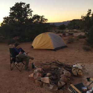 woman sits in camp chair reading by a firepit